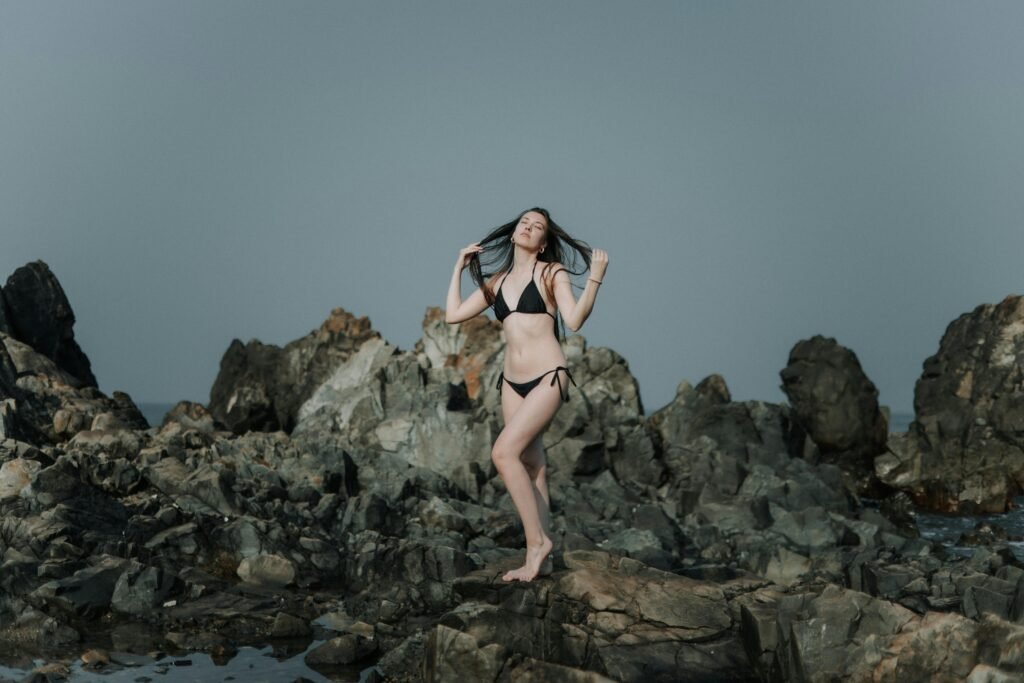 A young woman enjoys the seaside on rocky terrain during summer.
